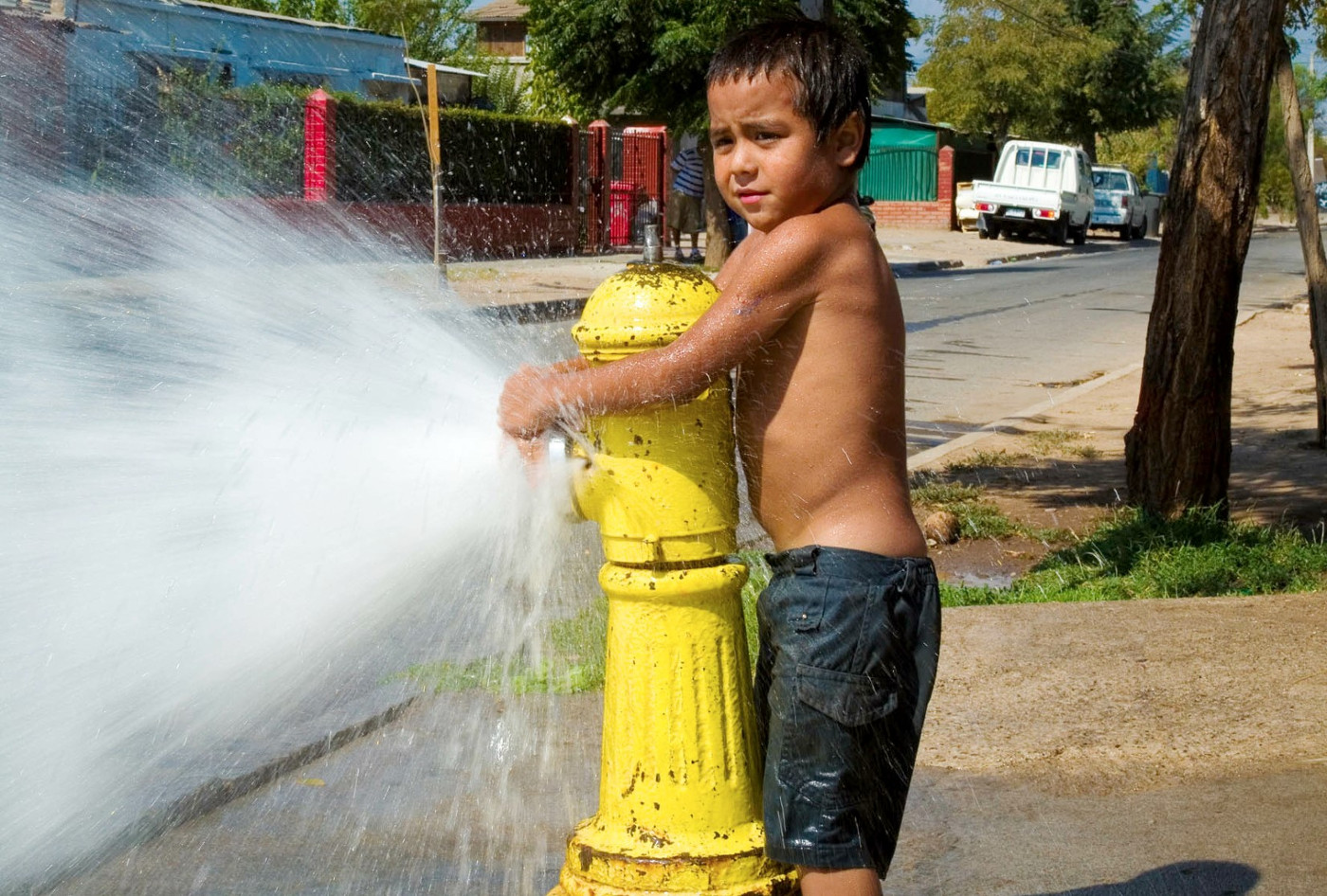 Ein Kind im Stadtrandviertel La Legua der chilenischen Hauptstadt Santiago spielt mit Wasser an einem Hydranten. Foto: Adveniat/Escher